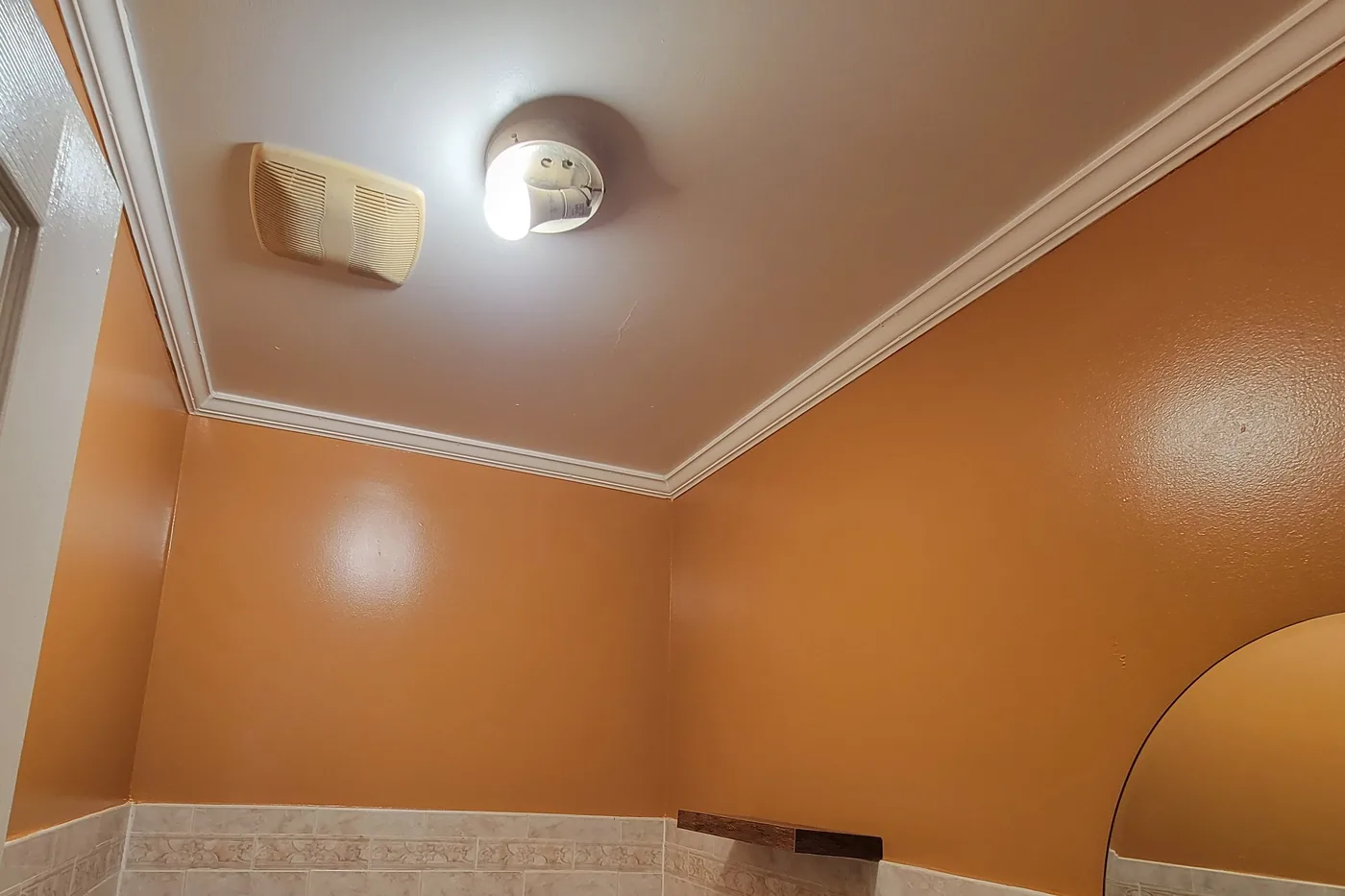 A bathroom after painting: warm ochre walls and a crisp white crown molding above the tiled wainscot.