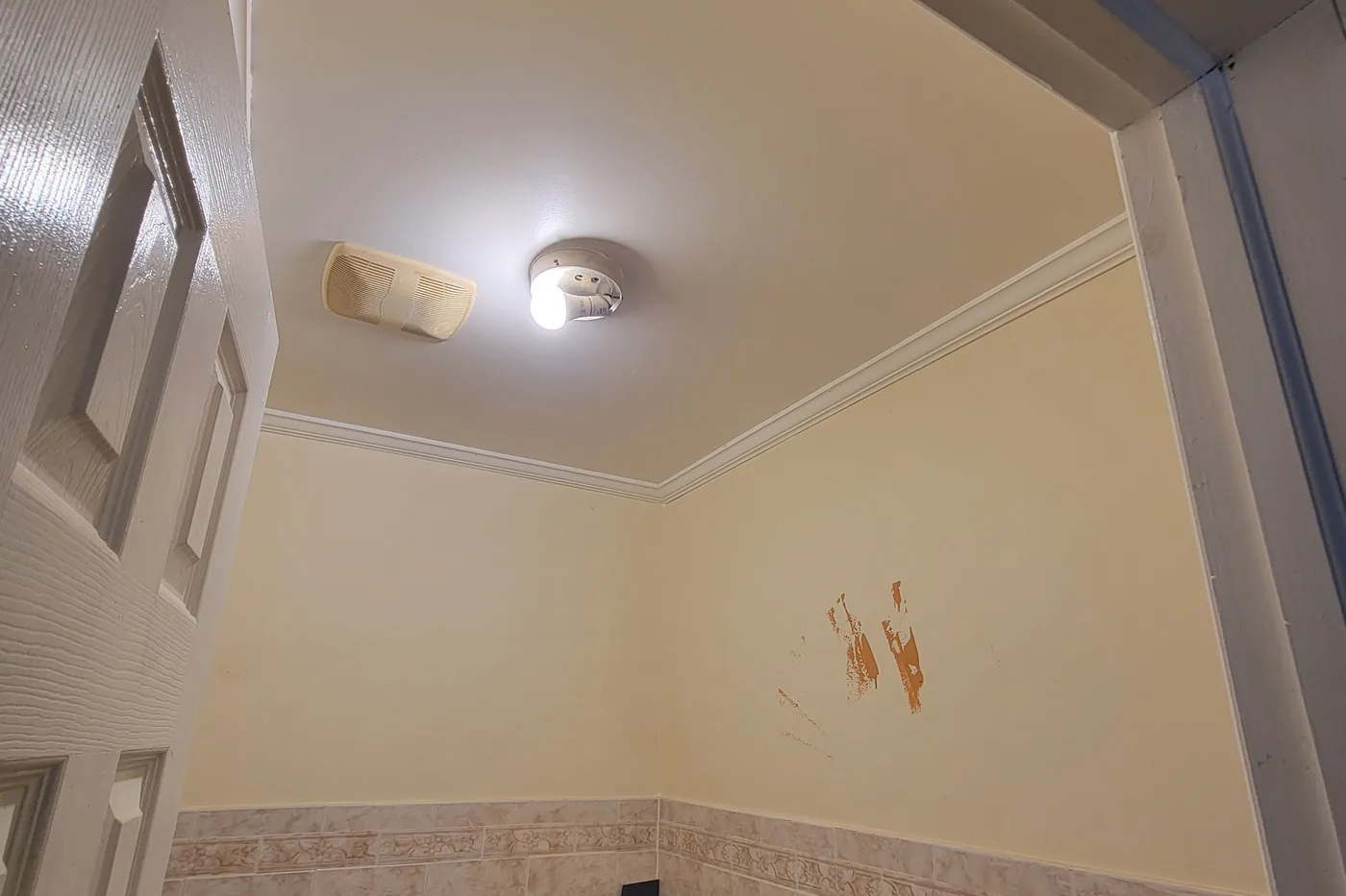The same bathroom before painting: dull cream walls with rust-colored staining above the tile.