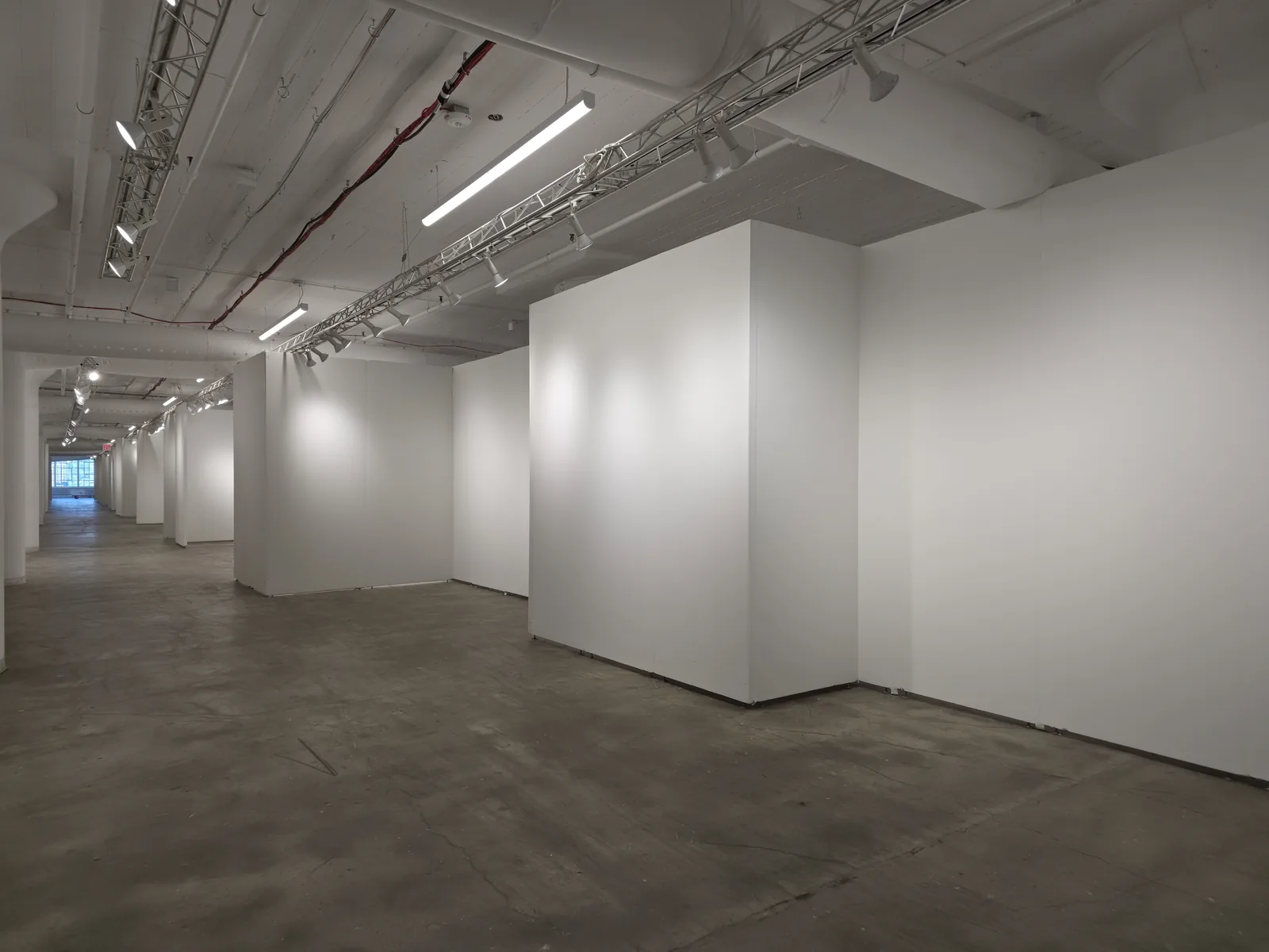 A Chelsea gallery floor: white partition walls under track lighting, the ceiling and ducts painted white above a bare concrete floor.