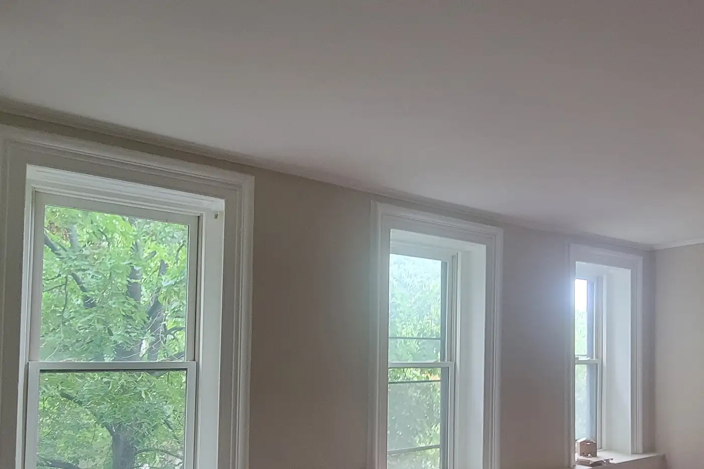 A Clinton Hill parlor after painting: warm greige walls with crisp white window casings and crown, three tall windows along the wall.