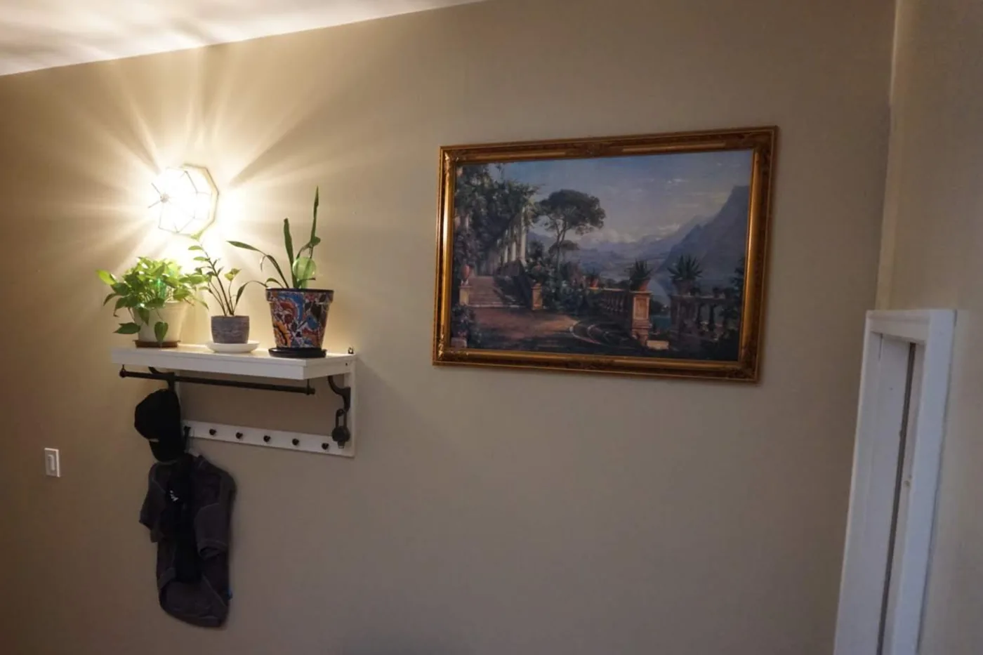 An entry wall after painting: one even warm gray, the shelf and framed picture back up, no patch left showing.
