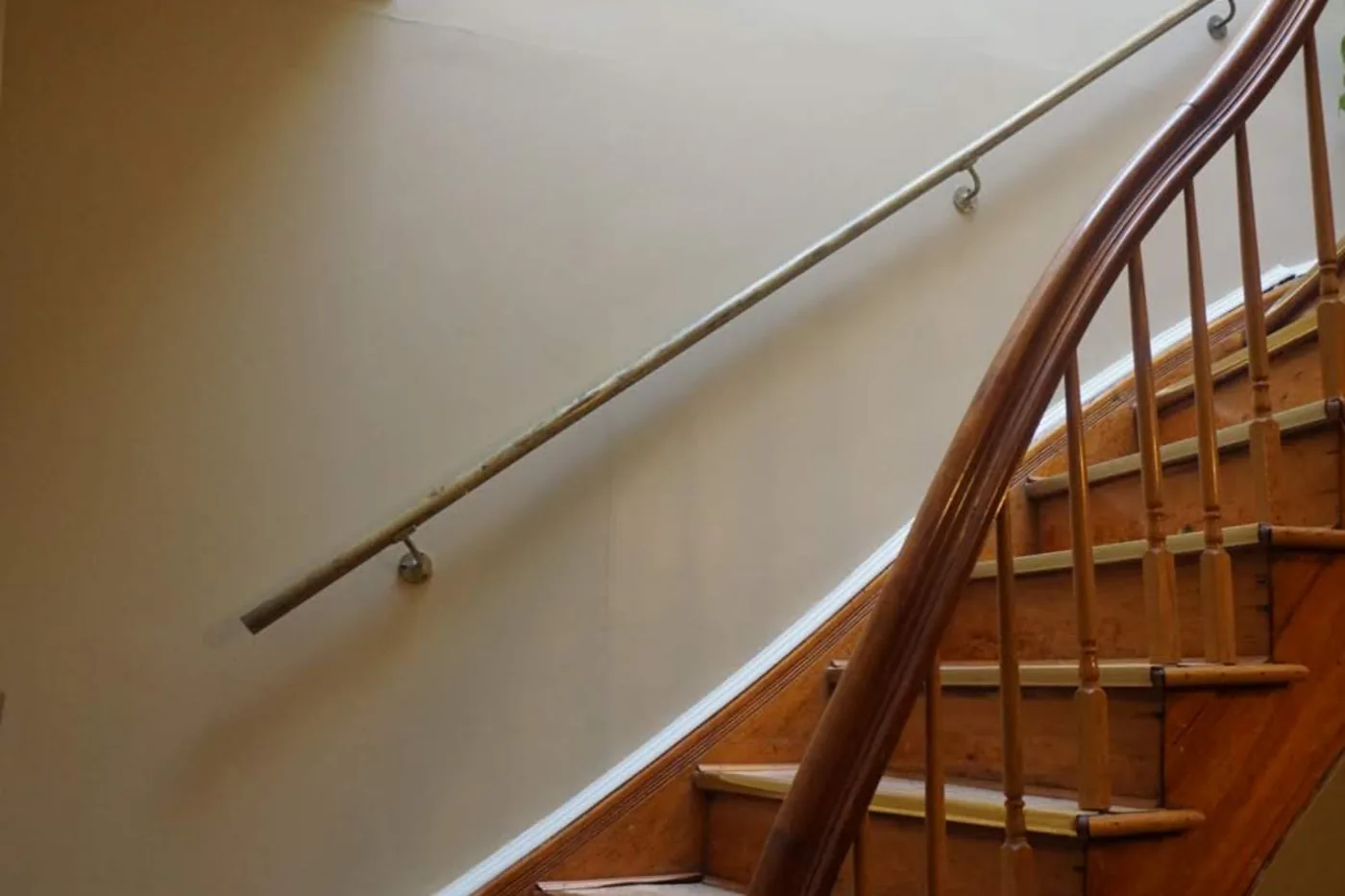 The stair hall after painting: an even cream wall meeting the white stair skirt in a clean line, original wooden banister.